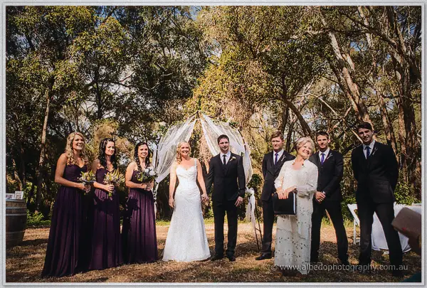 Bridal party and celebrant posing beneath the arch after the ceremony
