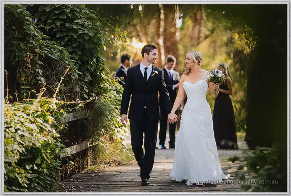 Newlyweds strolling hand in hand along a timber boardwalk in golden light
