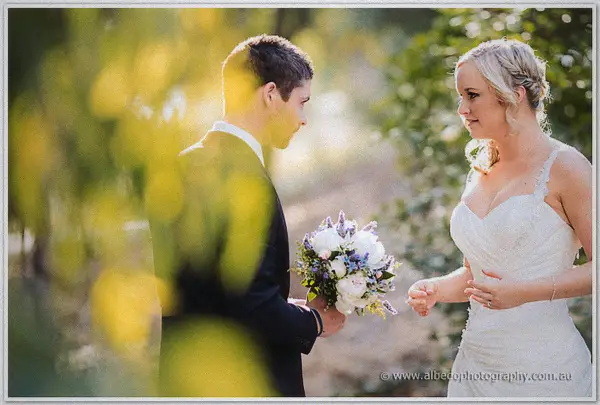 Payden presenting his bride with a white and lavender bouquet in dappled sun