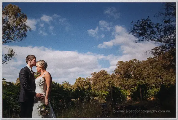 Ashley and Payden kissing in a vineyard beneath a wide summer sky