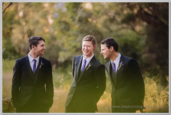 Groomsmen in charcoal suits sharing a joke in a sunlit bushland clearing