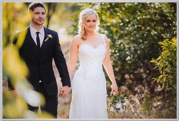 Bride and groom smiling at the camera on a leafy garden path