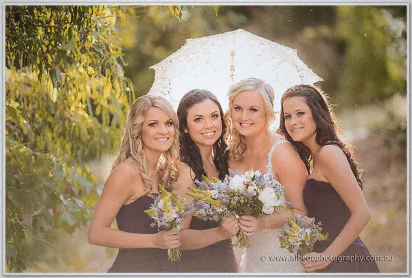 Bridesmaids sheltering under a lace parasol with the beaming bride