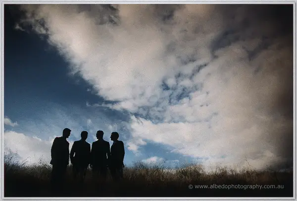 Groomsmen silhouetted against dramatic clouds in a golden field