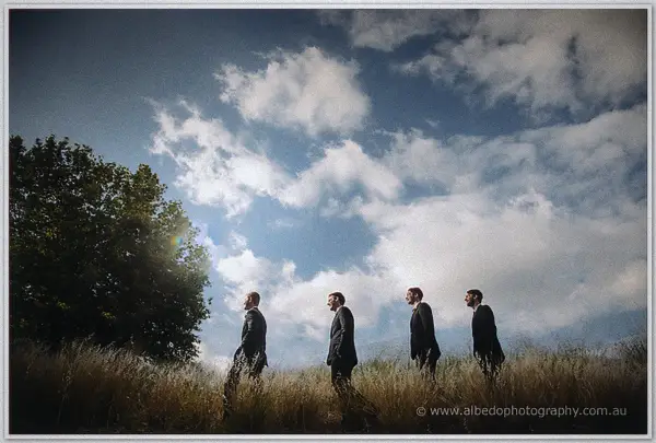 Groomsmen strolling single file through windswept paddock grass