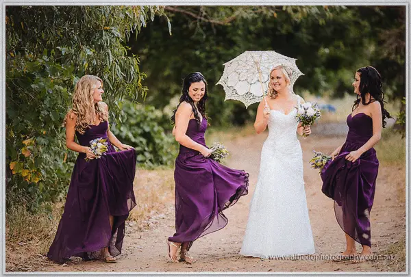 Bridesmaids twirling purple gowns beside the parasol-shaded bride