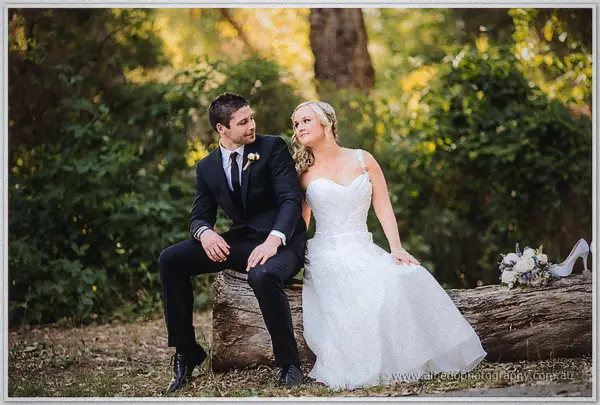 Ashley and Payden seated on a fallen log with her bouquet and heels