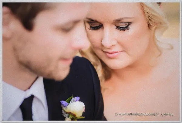 Close-up of the bride's lowered lashes beside the groom's white rose and lavender boutonniere