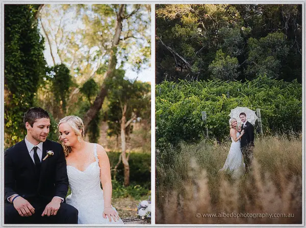 Newlyweds seated beneath leafy trees and shaded by a lace parasol in tall vineyard grasses