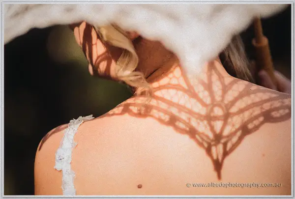 Lace parasol shadow patterning the bride's bare back in warm golden light