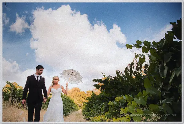 Ashley and Payden stroll hand in hand along a Carilley Estate vineyard row beneath towering clouds