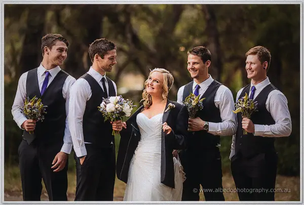 Ashley grins among her groomsmen in waistcoats, her jacket draped over one shoulder in the bush