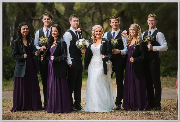 The full wedding party of Ashley and Payden poses together, bridesmaids in plum gowns and dark jackets