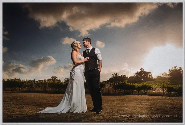 Ashley and Payden face each other on a lawn beneath dramatic clouds, her train sweeping the grass