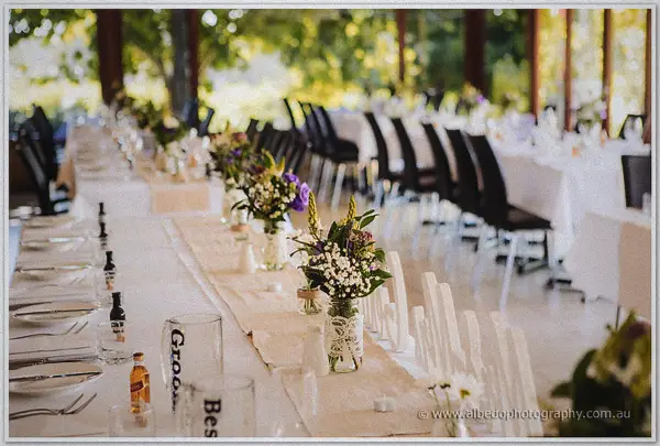Long reception tables dressed in white with wildflower jars and lace runners in garden light