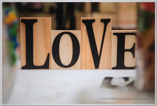 Wooden LOVE letter blocks in black type sit on a white tablecloth in soft reception light