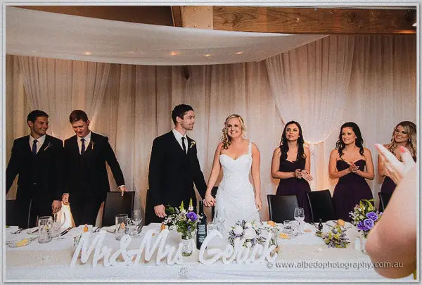Ashley and Payden join their bridal party at the head table under white draping and chandeliers