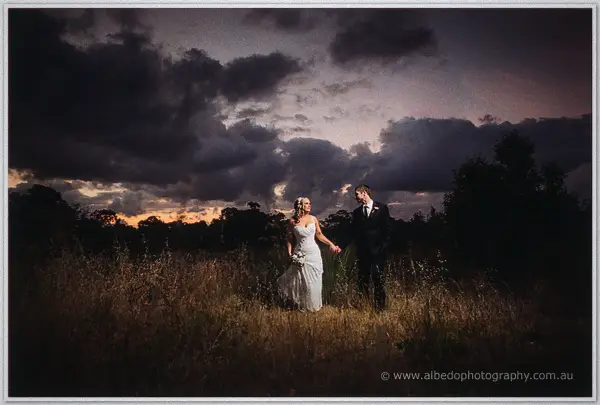 Couple strolls hand in hand through tall grass beneath heavy clouds at last light