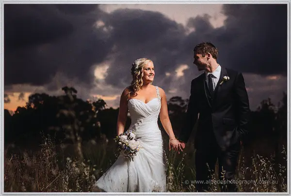 Ashley smiles up at Payden as they hold hands in a windswept paddock under moody dusk cloud