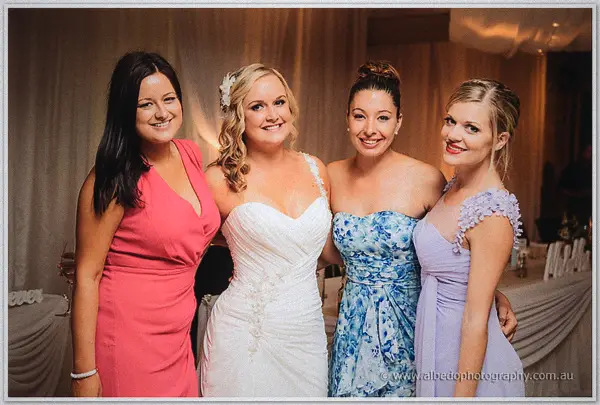 Ashley beams between friends in coral, floral blue, and lavender dresses at the reception