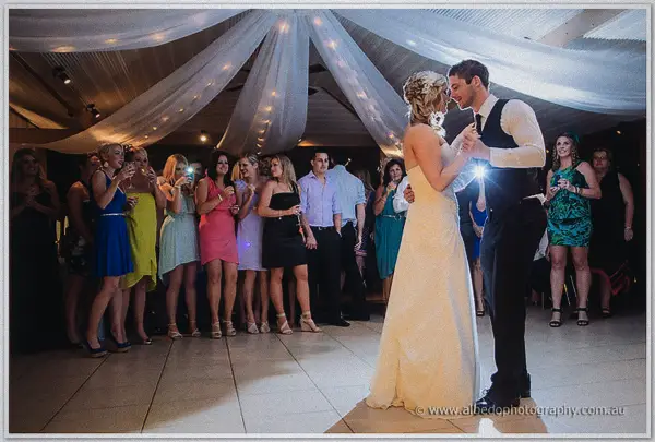 The newlyweds dance across the tiled floor while guests ring the floor with raised phones