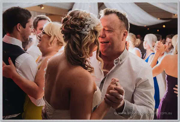 Ashley laughs while dancing with an older man in an open-collar white shirt among the crowd