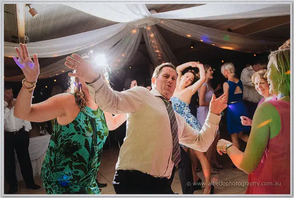 Guests dance with arms flung wide beneath draped fabric and fairy lights at the Carilley Estate reception