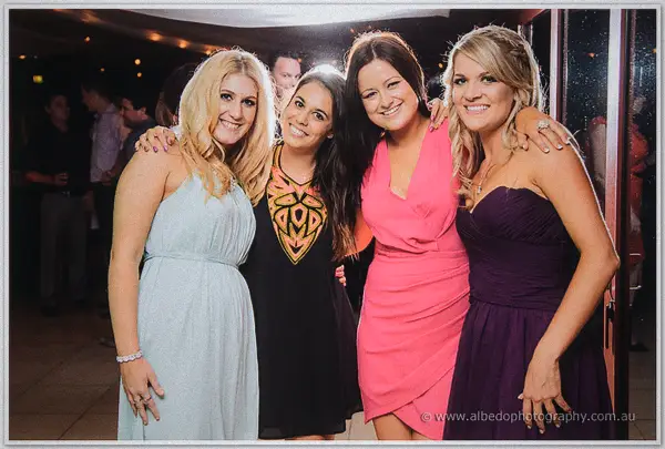 Four female guests in pastel dresses pose arm in arm and smile at the Carilley Estate wedding reception