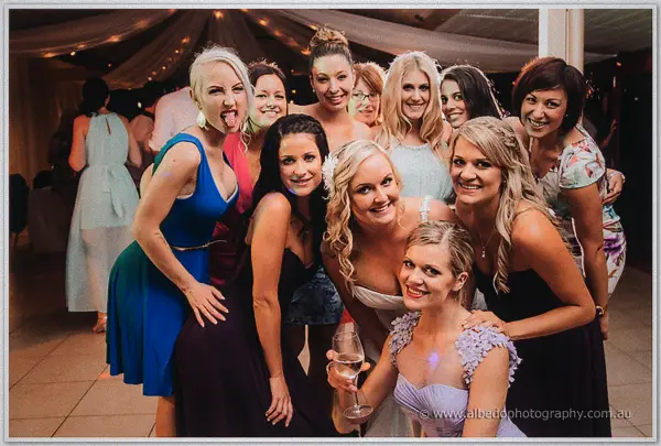 A crowd of female friends huddles around the laughing bride, champagne in hand, at Carilley Estate
