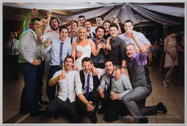 The bride is mobbed by cheering groomsmen and friends toasting with beers on the Carilley dance floor