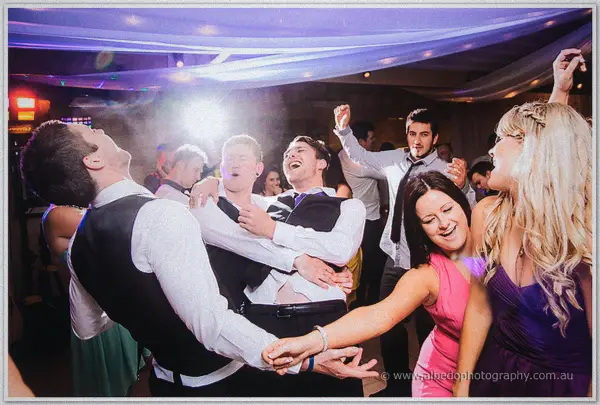 Dancing guests tip back in laughter as purple party light washes the Carilley Estate marquee