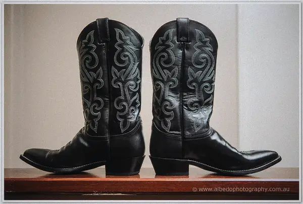 Pair of black embroidered leather cowboy boots waiting on a polished timber shelf