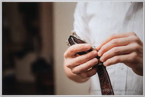 Close-up of hands fastening an engraved buckle on an embossed leather belt in soft window light