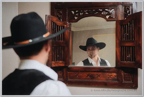 Gary checks his reflection in a carved timber mirror, black cowboy hat and vest in place