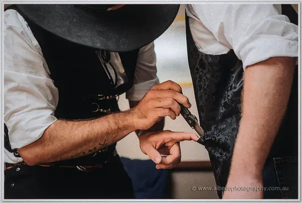 A groomsman in a black hat clips a bolo tie clasp onto Gary's vest before the ceremony