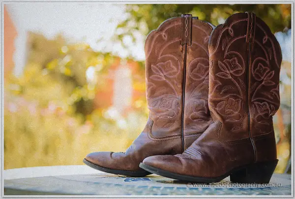 Pair of embroidered tan leather cowboy boots resting on a sunlit veranda ledge