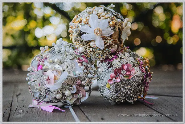 Three brooch-and-pearl bouquets cluster together on weathered timber boards in the garden