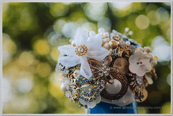 Close-up of Tash's heirloom bouquet of brooches, pearls and fabric flowers against dappled green