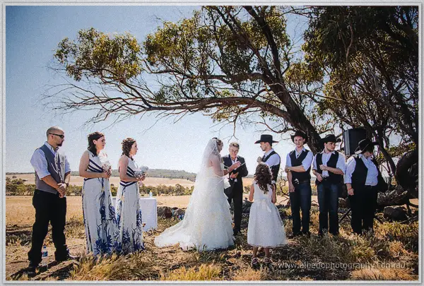 Tash and Gary exchange vows in the open paddock, flanked by their bridal party beneath a sprawling gum tree.