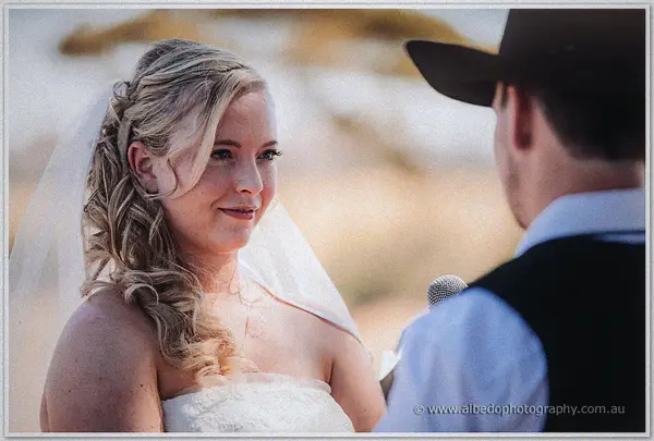 Tash gazes at Gary over a microphone during their vows, her curled hair catching the afternoon light.