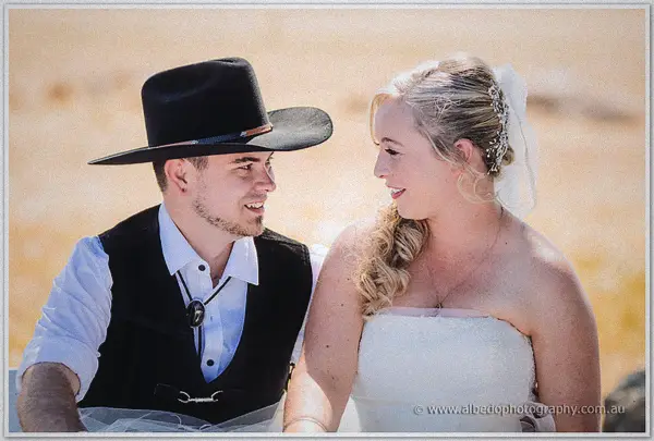 The newlyweds beam at each other in the golden paddock, his black hat tipped beside her soft curls.
