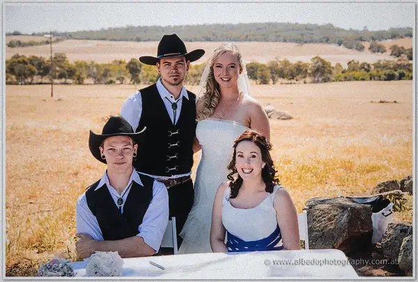 The signing party of four beams at the white-clothed table flanked by hat-wearing witnesses.