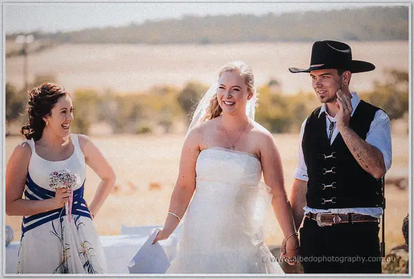 Laughter erupts as the maid of honour walks the laughing newlyweds back across the dry paddock.