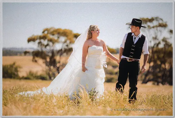 Tash's long veil trails through golden grass as the couple stroll past gnarled gums in the midday sun.