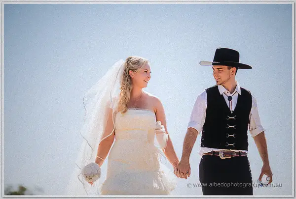 Tash and Gary walk hand in hand under a huge pale sky, her veil and his black hat catching the light.