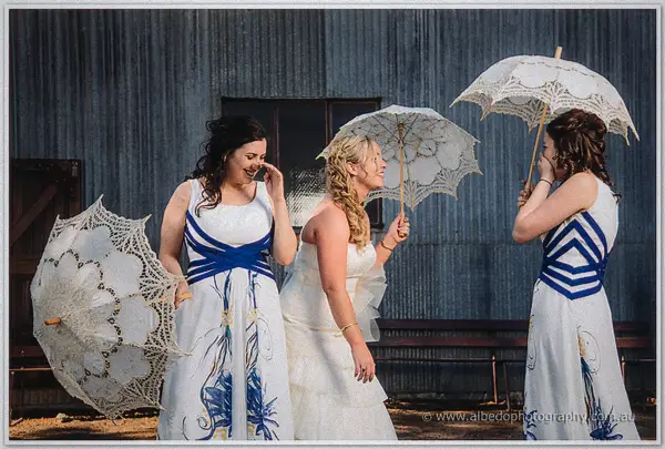 Bridesmaids giggle behind parasols as Tash spins in her ruffled gown outside the grey shearing shed.