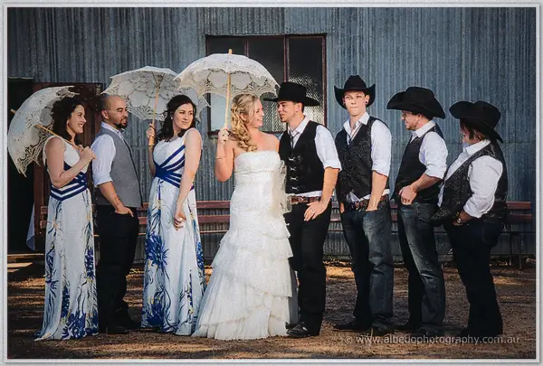 The whole wedding party lines up before the tin shed, bridesmaids with parasols and groomsmen in cowboy hats.