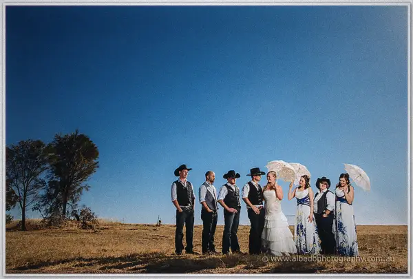 A wide shot of the couple and their party standing along the fence line beneath an immense cobalt sky.