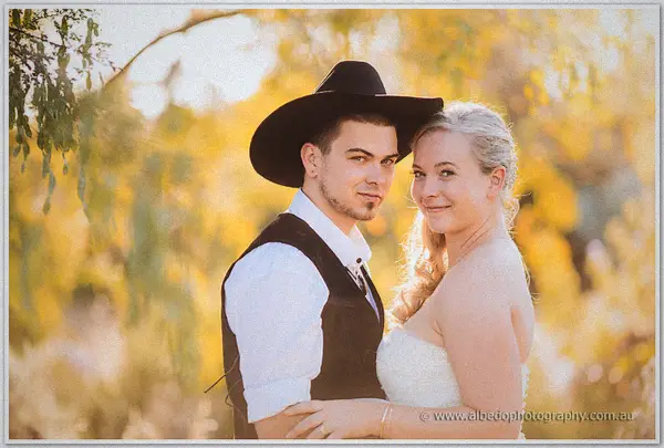 Close-up of Gary in his black hat beside beaming Tash, golden foliage blurring behind them