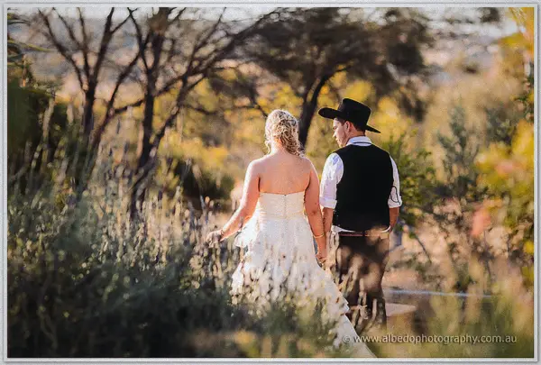 Tash and Gary walk hand in hand down a sandy bush track, backlit by low golden afternoon sun